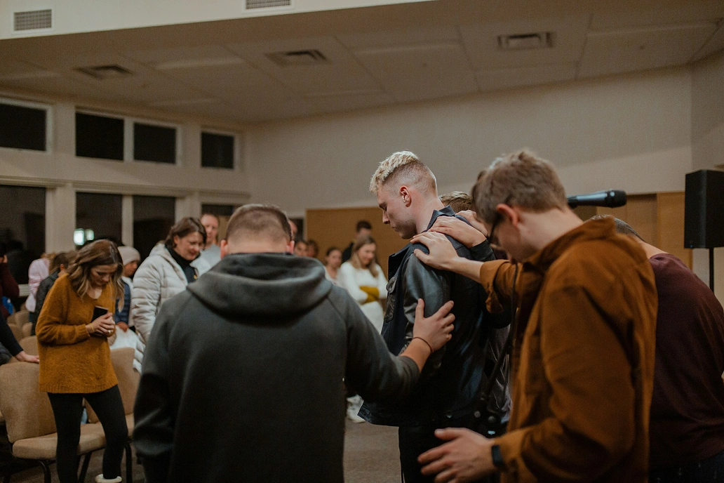 Young man receiving prayer while surrounded by people laying hands on him at church.