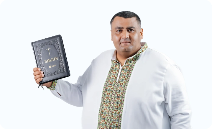 A man in an embroidered Ukrainian shirt holds up a Bible, possibly a leader in his church.
